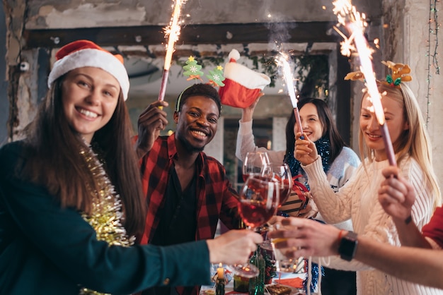 Multi-ethnic friends toasting wine. Young men and women having a party in cafe. Christmas.