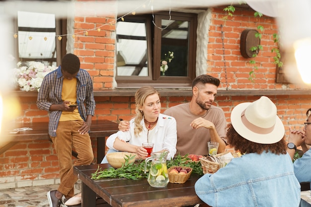 Multi-ethnic group of beautiful young people enjoying dinner outdoors in sunlight while sitting at wooden table