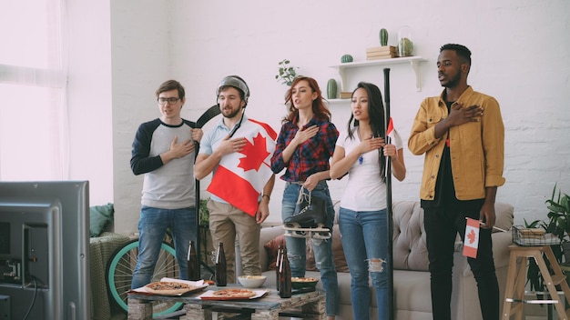 Multi ethnic group of friends listening and singing national Canadian anthem before watching sports