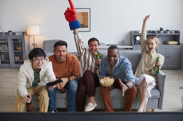 Multi-ethnic group of sports fans watching game match at home and cheering joyfully raising hands , copy space