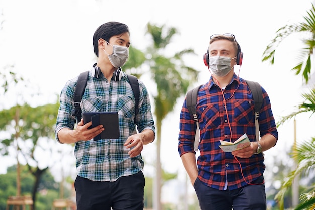 Multi-ethnic young people with backpacks walking in the street with medical maksks on faces