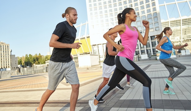 Multi racial young sportsmen running along sunny city