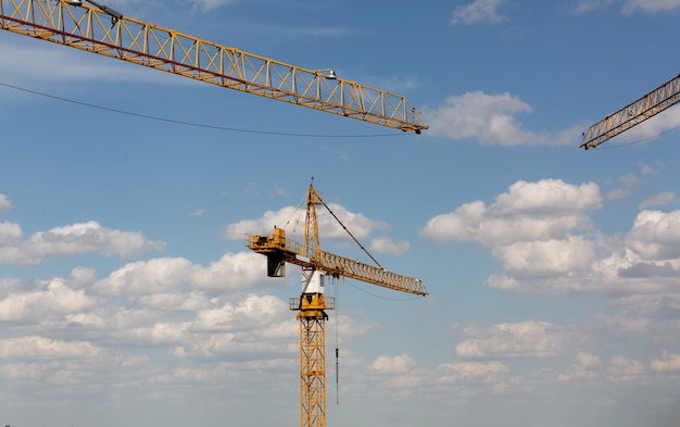 Multi storey building concept: tower cranes at the construction site at the sky and clouds background