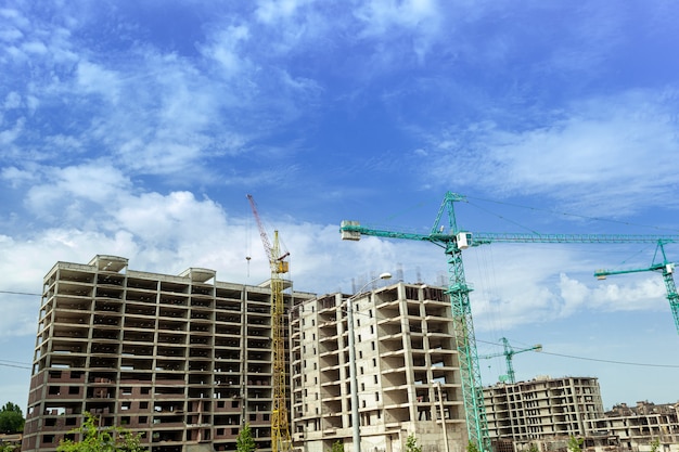 Multi-storey residential building under construction and crane on a background of blue sky