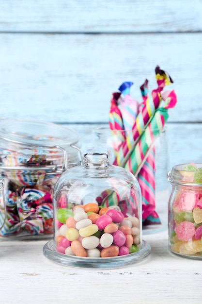 Multicolor candies in glass jars on color wooden background