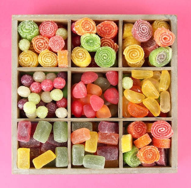 Multicolor candies in wooden box on color background