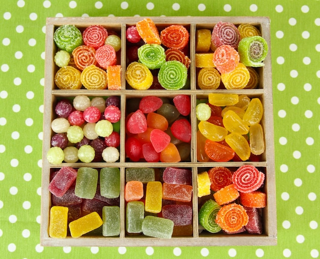 Multicolor candies in wooden box on color background