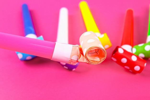 Multicolor party blowers on pink color. Multicolored party whistles. Decor for a birthday.