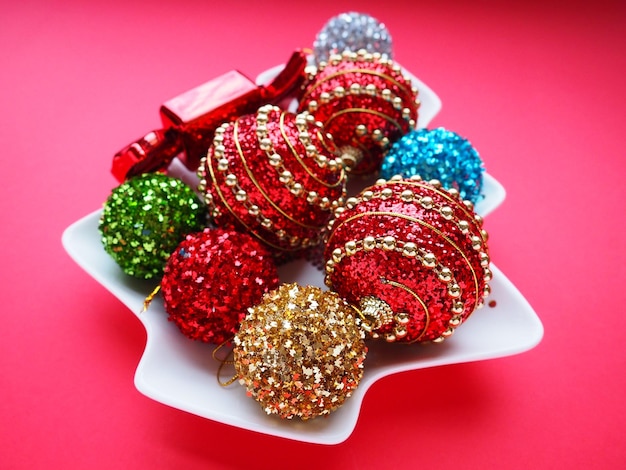 Multicolored Christmas balls and candies on a white plate in the shape of a Christmas tree Red pink background Beautiful striped red pink green silver yellow blue gold Christmas decorations