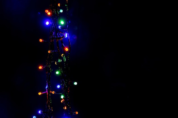 Multicolored Christmas and New Year garland lights on a black background vertically copy space