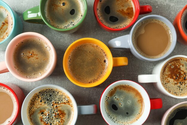 Multicolored cups of coffee on grey table as background