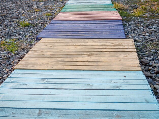 Multicolored decking on a pebble beach The path to the shore from different colored boards