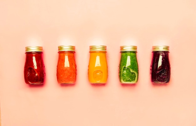 Multicolored detox vegan vegetable juices and smoothies in glass bottles on pink table raw diet....