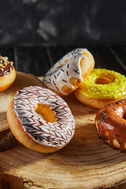 Multicolored donuts with glaze and sprinkles on wooden coasters on a black background.