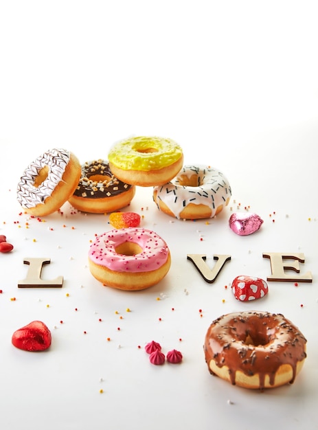 Multicolored donuts with icing, sprinkles and the inscription love on a white background.