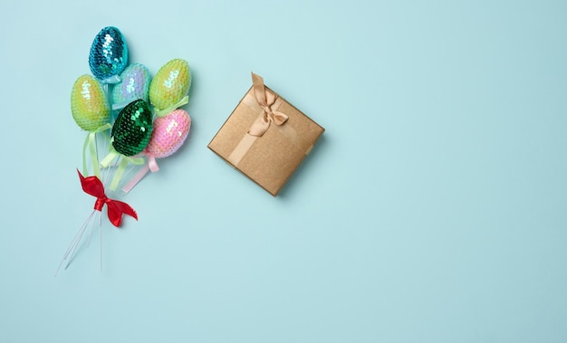 Multicolored Easter decorative eggs in sequins and a gift on a blue background View from above