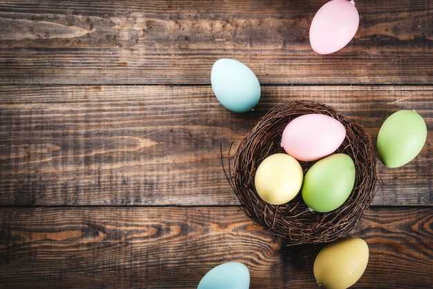 Multicolored Easter eggs in bird's nest on wooden table, copy space top view