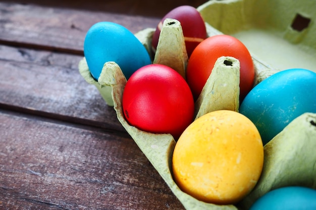 Multicolored eggs painted with gouache and onion peel in a cardboard box on a wooden table background Ten boiled eggs Postcard poster for Easter Easter holiday Red blue yellow brown eggs