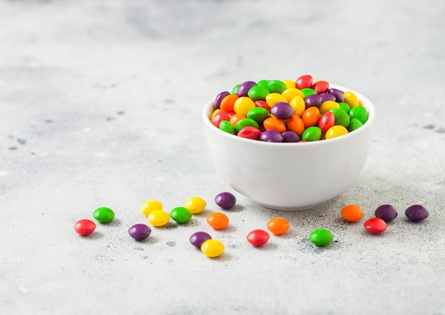 Multicolored fruit candies in white bowl on light background