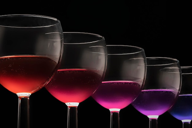 Multicolored glasses with different wines coctail purple blue red on a black background glasses in a row