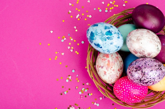 Multicolored handmade easter eggs and confetti on pink background. Minimal concept. View from above. Space for text. Studio Photo