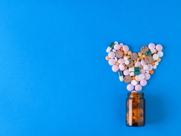 Multicolored heart-shaped pills pour out of a glass brown bubble on blue.