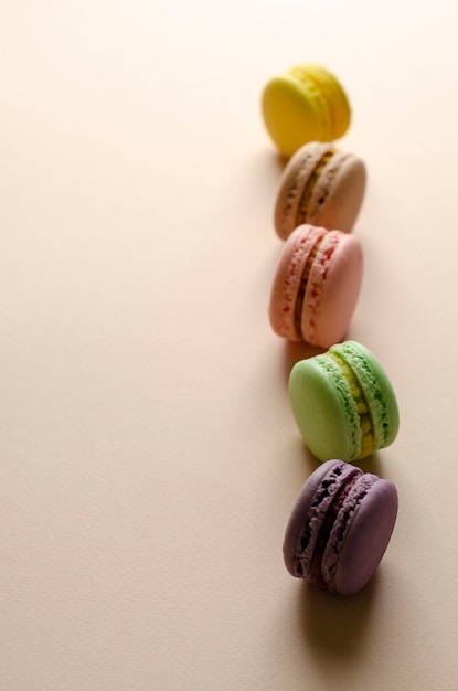 Multicolored macaroons in a row on pastel beige