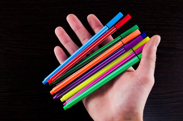 Multicolored markers in a hand on a dark background table