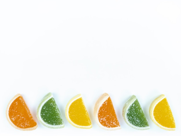 Multicolored marmalade citrus slices in sugar on a white background with copy space.