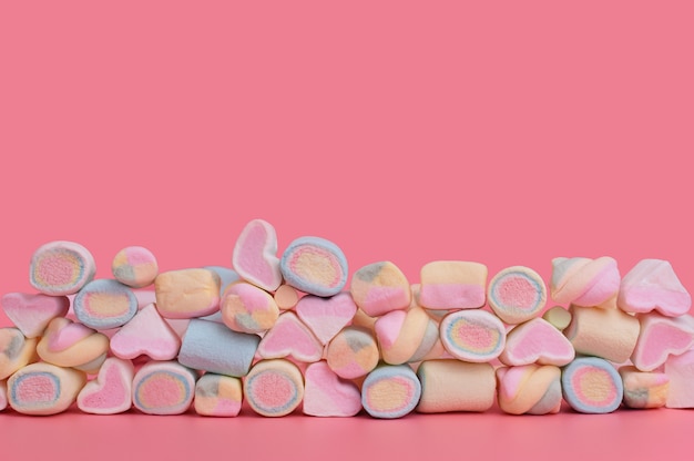 Photo multicolored mixed marshmallows in several rows on a pink background. sweets on pink with place for text.