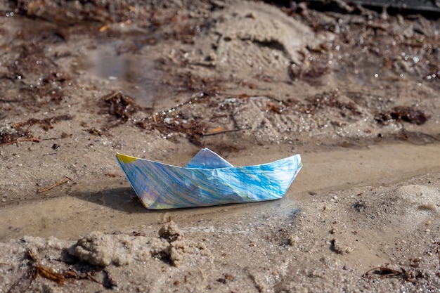 Multicolored origami paper boat in stream or puddle A symbol of childhood or piece of light in dark world