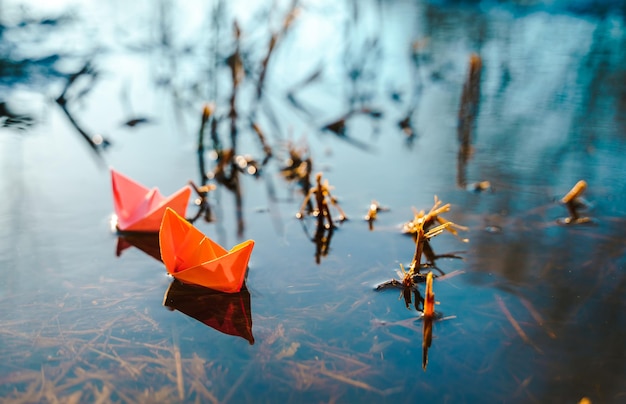 Multicolored paper boats Colorful pink yellow blue orange ships in big spring snow puddle on winter street Warm wet rainy weather old grass Hello spring autumn Children play have fun outdoors