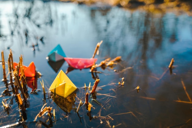 Multicolored paper boats Colorful pink yellow blue orange ships in big spring snow puddle on winter street Warm wet rainy weather old grass Hello spring autumn Children play have fun outdoors