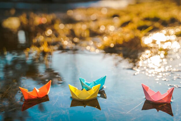 Multicolored paper boats Colorful pink yellow blue orange ships in big spring snow puddle on winter street Warm wet rainy weather old grass Hello spring autumn Children play have fun outdoors