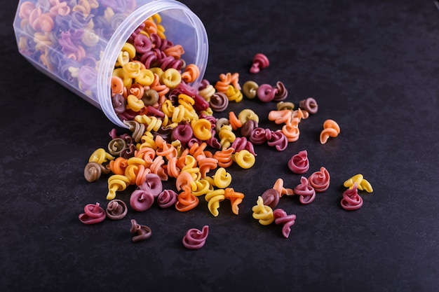 Multicolored pasta with the addition of natural vegetable dye. Scattered from a can on a black concrete table