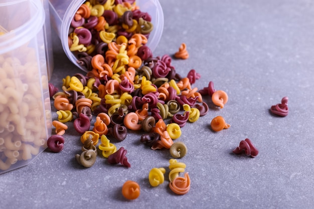 Multicolored pasta with the addition of natural vegetable dye. Scattered from a can on a concrete table