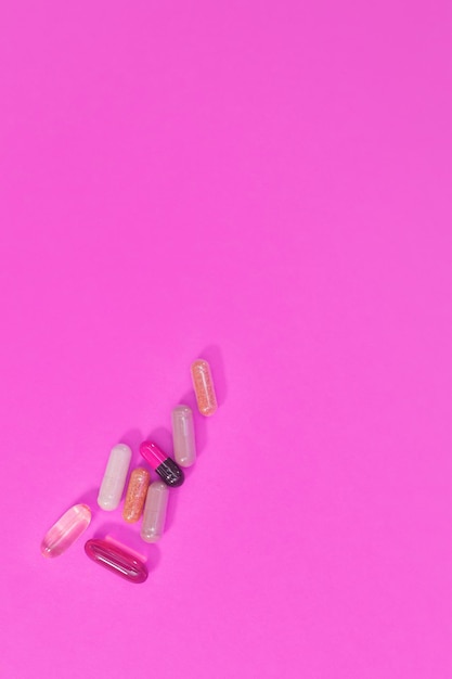 Multicolored pills and capsules on a pink background