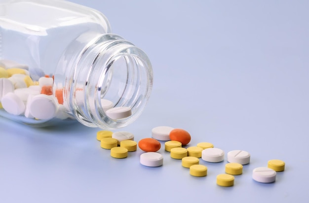 Multicolored Pills spilling out from transparent glass medicine bottle Copy space