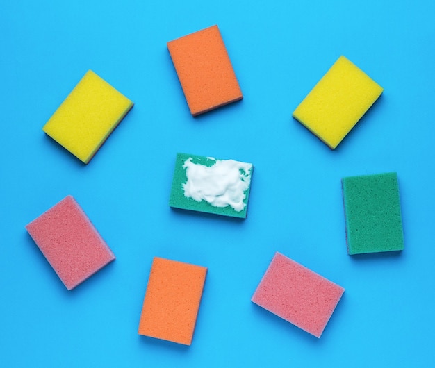 Multicolored set of bright foam sponges on a blue background Minimal concept of washing and cleaning