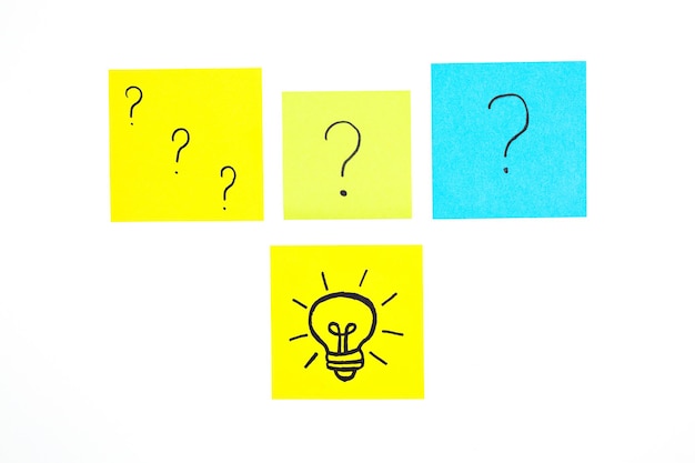 Multicolored sheets of note paper with painted question marks and a light bulb on a white background