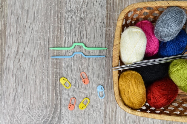 Multicolored skeins for knitting in a basket on a wooden background Place for an inscription Knitting tools knitting needles markers auxiliary knitting needles Knitting