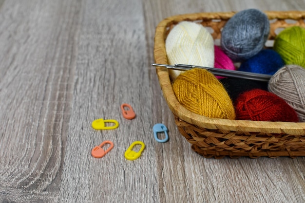 Multicolored skeins of thread for knitting in a basket on a wooden background Place for an inscription Iron knitting needles markers Knitting