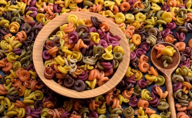 Multicolored spiral raw pasta fusilli in a wooden bowl