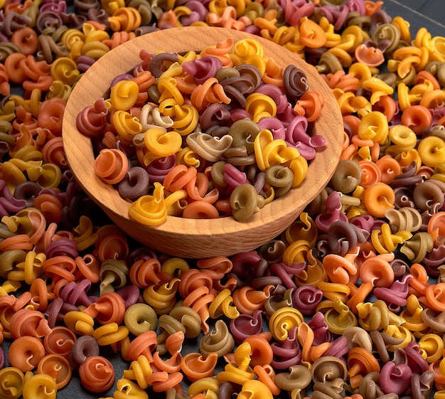 Multicolored spiral raw pasta fusilli in a wooden bowl