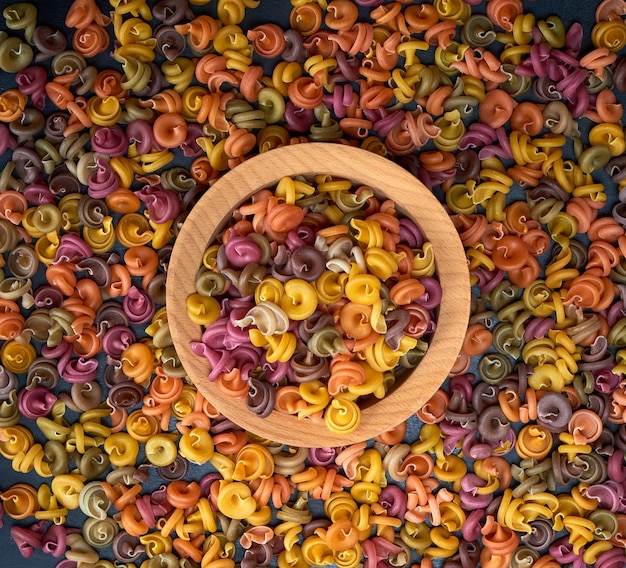 Multicolored spiral raw pasta fusilli in a wooden bowl