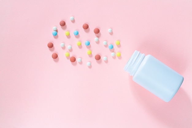 Multicolored tablets pills capsules in plastic bottle on pink background copy space