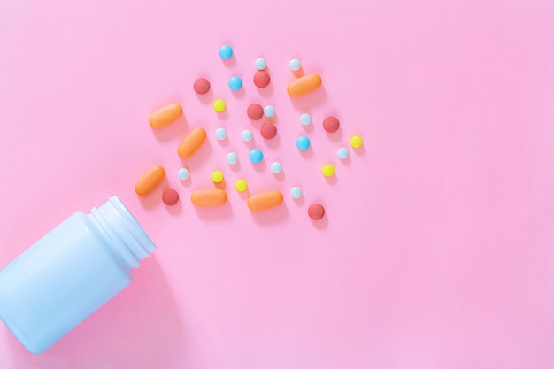 Multicolored tablets pills capsules in plastic bottle on pink background copy space