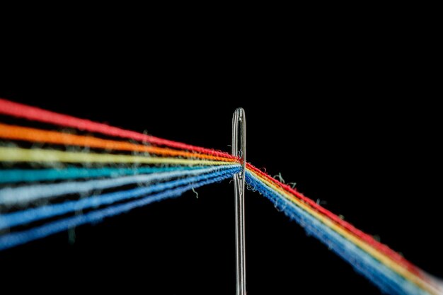 Multicolored threads for sewing in the form of a rainbow pass through an antique needle on a black background