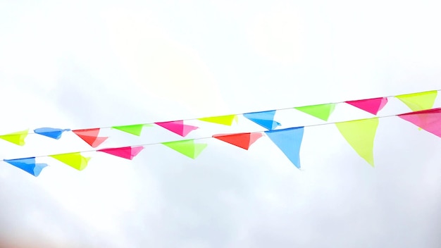 Multicolored triangular flags hang on a string and flutter in the wind against a cloudy cloudy sky