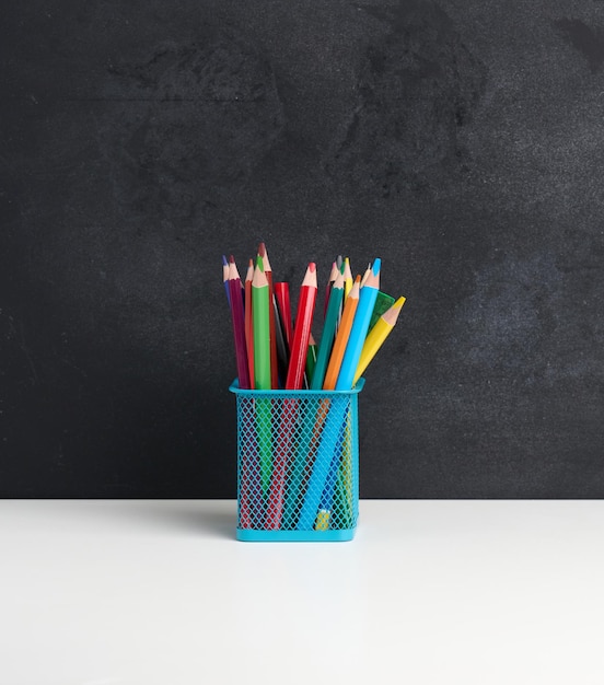 Multicolored wooden pencils in a metal basket on a black chalk board background